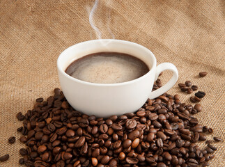 Cup of coffee on a saucer with coffee beans on a background of burlap