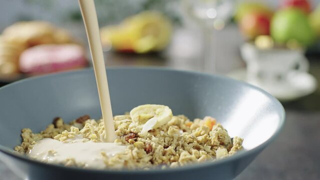 Pouring yogurt into a plate with muesli. Healthy dry breakfast. Granola with fruit in the morning, porridge with fruit and dried fruit in the morning. High quality 4k footage