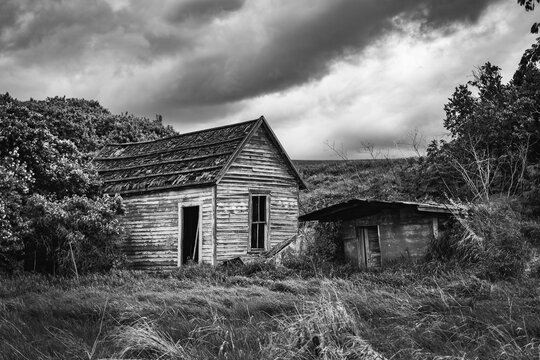 Black and white image of a spooky old abandoned house under threatening weather clouds in Eastern Washington, USA; Colfax, Washington, United States of America