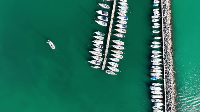 MONFALCONE, ITALY - APRIL, 2023: Sailing yacht moored off the coast Adriatic sea in Italy at sunny day. Drone aerial view, cinematic frame. Romantic atmosphere. Calm and pacifying scene.