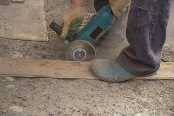 a man saws off the edge of a wooden board with a grinder - obrazy, fototapety, plakaty