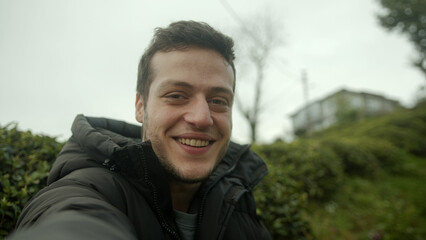 Young Brown-Haired Man in a Black Jacket Conducts a Video Conference Against a Beautiful Nature House Background - POV Shot