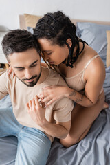 Fototapeta premium high angle view of bearded man touching hand of hot african american woman in lingerie in bedroom at home.