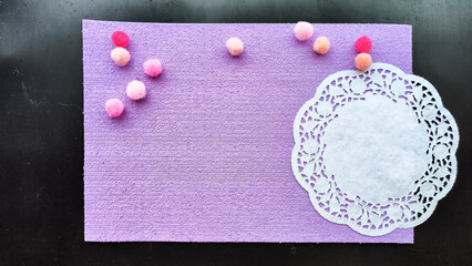 Top view of lilac or purple sheet of velvet paper, white carved napkin and color ball. Abstract frame, background and texture with copy space. Empty rectangle with round paper napkin on black colour
