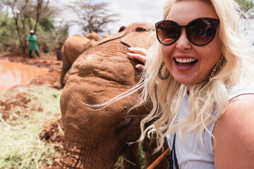 Happy laughing woman gets a photo taken as she pets a baby elephant