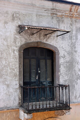 Neglected Old Balcony with Dark Grey Wooden Doors, Black Metal Railing, and Plain Concrete Wall