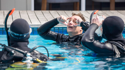 Scuba dive instructor teaching and explaining to students clearing your dive mask skills in the pool with his head tilted back