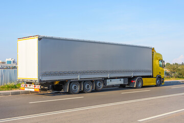 Truck yellow with a large trailer under an awning stop on the side of the road.