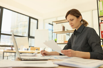 Woman with ponytail checks information making notes on paper