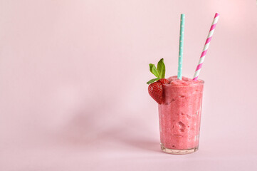 Strawberry smoothie in a glass with straw mint and strawberries on a pink background. Daylight with copy space for text