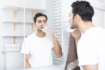 Handsome man looking at the mirror and shaving in the bathroom	