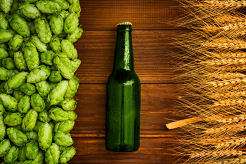 A bottle of beer on a wooden background with green hops and wheat ears