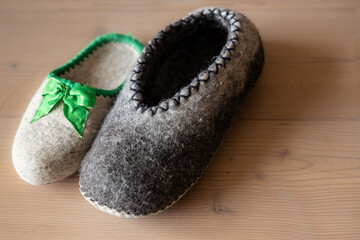 Unpaired men's and women's home shoes made of dried wool stand on a wooden floor
