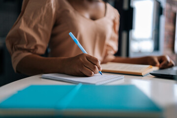Detail cropped shot of unrecognizable African American female student using laptop and paper book...