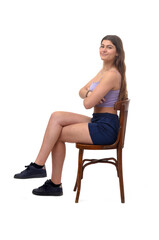 side view of a young girl sitting on chair looking at camera and cross legged and arms crossed on white background