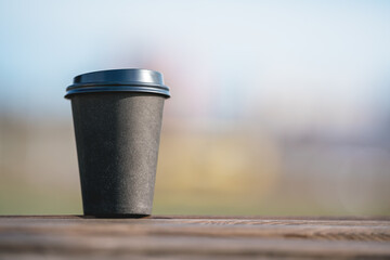 Obraz na płótnie Canvas Paper coffee cup with blank mockup space stands on wooden floor against blurry nature background close up front view.