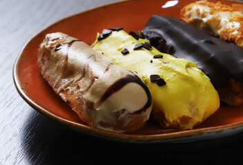 Classic French eclairs of oblong shape with various fillings and chocolate, mango, fruit creams on them. Close-up
