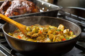 Wooden spoon with stewed vegetables in spices over a frying pan.
