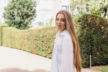 Attractive brunette woman walk on the countryside street. Girl wear white shirt and top and look happy and smiles. Woman walk on the street, she turn around and look joy.