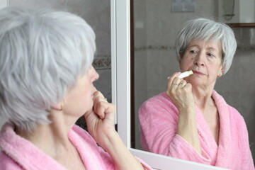 Senior woman moisturizing her lips in the bathroom 