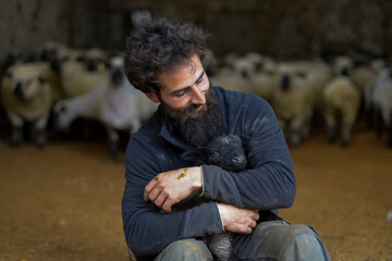 portrait of a breeder with a lamb in his arms inside a barn