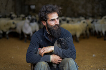 portrait of a breeder with a lamb in his arms inside a barn