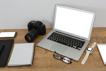 Laptop, wristwatch, notepad, camera and mobile phone on wooden table