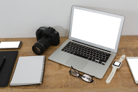 Laptop, wristwatch, notepad, camera and mobile phone on wooden table