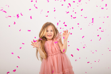 Obraz na płótnie Canvas little girl blonde in a pink dress catches confeti smiling happy on white background, holiday concept. A child is celebrating a birthday on a white background