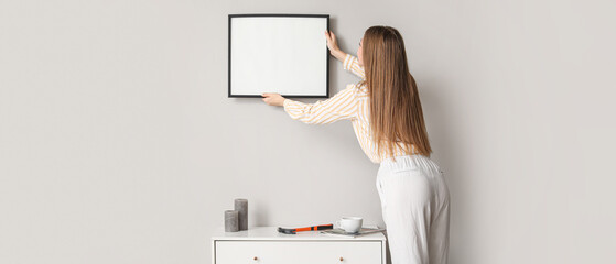 Young woman hanging blank picture on wall in room