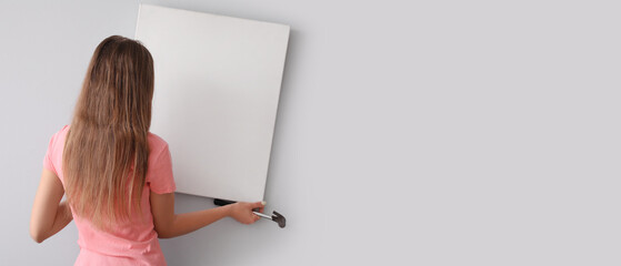 Young woman hanging blank picture on light wall at home, back view