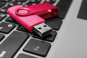 Pink USB flash drive on modern laptop, closeup