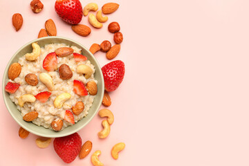 Bowl with tasty oatmeal, almonds, strawberries and hazelnuts on pink background