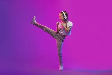 Tuinposter Sweet preteen child girl using wireless headphones and doing karate © Prostock-studio