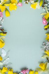 Spring flowers flat lay frame composition on colored background with copy space. Daffodils and willow with carnations top view