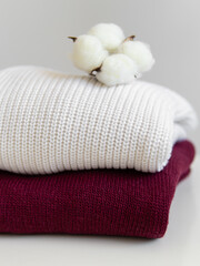 Two knitted sweaters and cotton flower on white background. Vertical. White and vinous sweater