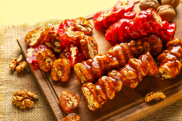 Board with delicious churchkhela and walnuts on yellow background