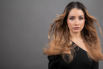 Obraz premium Developing female hair. Beautiful young female model with flowing hair, looks atcamera on gray background. 