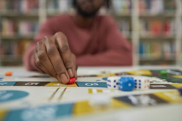 Fototapeta premium Closeup of black man playing board game with focus on male hand moving game piece, copy space