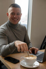 Handsome joyful man drink coffee in cafe. Happy business man working on notebook sitting at table in coffee house.