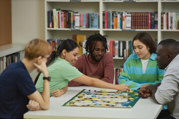 Multiethnic group of young people playing board games together while sitting around table in...