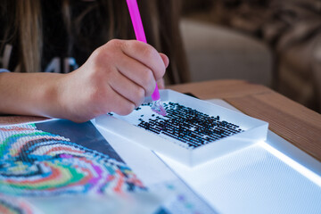 Little girl making diamond painting or pearl mosaic picture. Colorful small pearls stick on image on canvas. Photo series. Trending calming kids leisure activity.