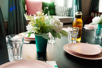 Table setting for a wedding or another catered event dinner party or children birthday party. Interior design in soft pastel green and pink colors. Artificial flowers in paper cup.