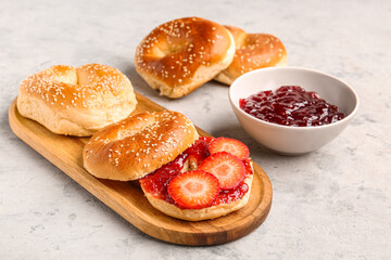 Wooden board of tasty bagels with sesame and strawberry jam on grunge background