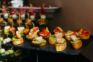 catering wedding buffet with different food snacks and antipasti. shrimps with avocado spread, bruschetta with salmon and lemon wedges.