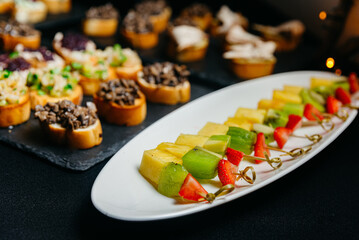 Catering food. Canapes with fruits and berries on skewers. Variety of snacks.