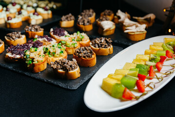 catering food on a black background. fruit canapes and veggie appetizers. many portions, catering buffet.