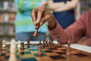 Close up of black young man playing chess with focus on male hand moving chess piece
