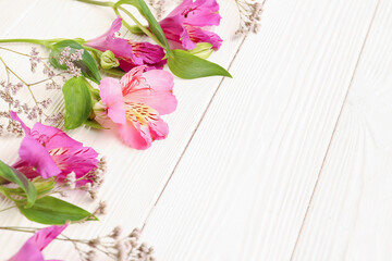 Pink alstroemeria with gypsophila flowers on white wooden background