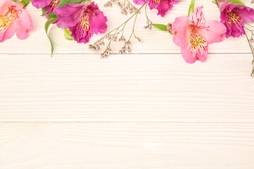 Pink alstroemeria with gypsophila flowers on white wooden background